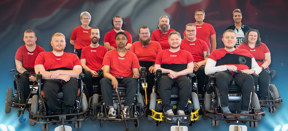 Photo of the Danish National team of Powerchair Hockey with a danish flag and spotlights in the background.